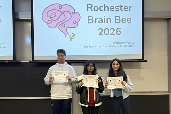 Three people holding certificates while smiling at the camera with a slide show in the background.